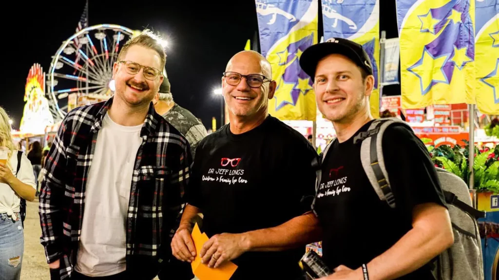 3 men wearing black shirts smiling at the camera at the Tulsa fair