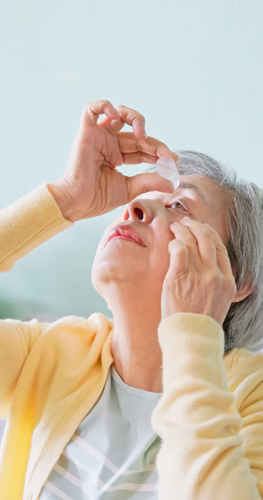 mature woman wearing a yellow sweater applying eye drops